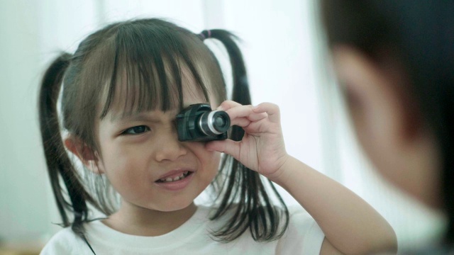 慢镜头泰国可爱的小女孩在镜子前玩相机玩具，同时笑着，情绪积极视频素材