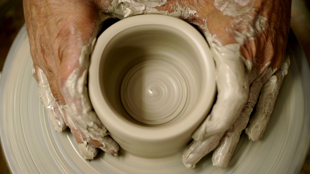 人们用未加工的湿粘土在制陶轮上制作了一个手臂脏兮兮的罐子视频素材