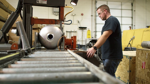 一位三十多岁的白人技术员在室内制造设施中使用一个大型工业锯子切割一个旋转成型的钢鼓视频素材