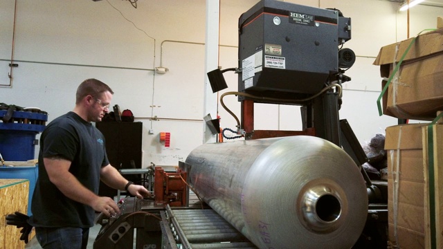 一位三十多岁的白人技术员在室内制造设施中使用一个大型工业带锯切割一个旋转成型的钢鼓视频素材