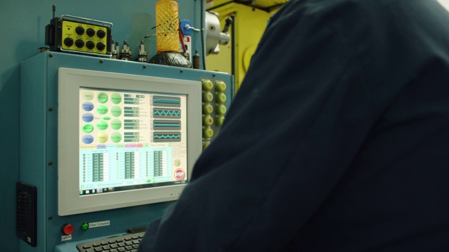 一位三十多岁的白人技术员戴着防护眼镜在室内制造工厂里操作电脑视频素材