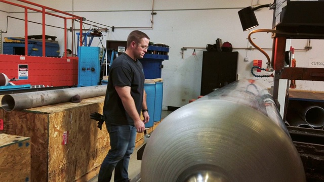 一位三十多岁的白人技术员在室内制造设施中使用一个大型工业锯子切割一个旋转成型的钢鼓视频素材