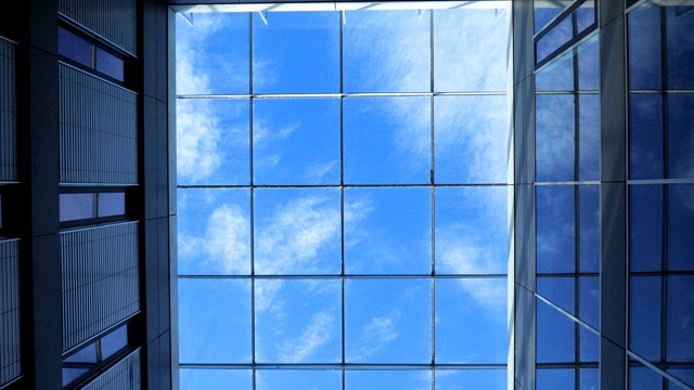 云和鸟在蓝天中缓慢移动的画面。透过玻璃天花板向上看。视频下载