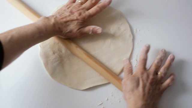 年长妇女在厨房柜台上用擀面杖擀面，为制作披萨或传统派做准备视频素材