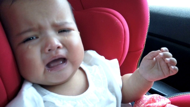 悲伤的婴儿在驾驶途中在红色的汽车座椅上哭泣视频素材