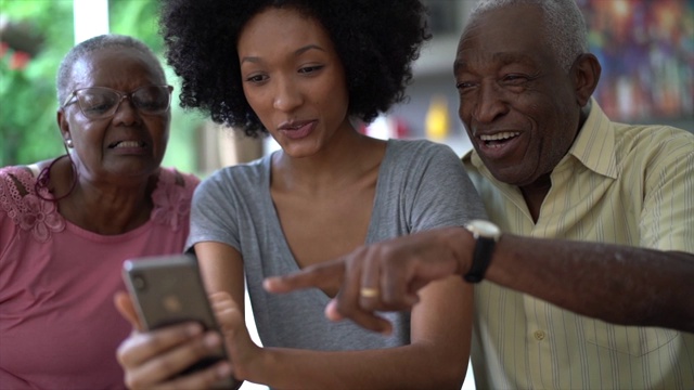 一个女人向一对老年夫妇展示手机，人们微笑着玩视频下载