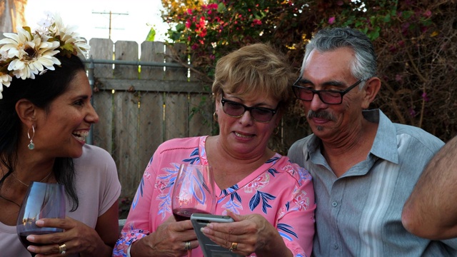 成年家庭成员在后院烧烤时笑着看智能手机上的视频视频下载