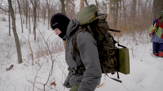 白天，两名男性和两名女性徒步旅行者在冬日的森林里漫步，用树枝自取食物视频素材