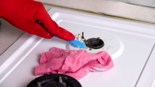 女人戴着红色橡胶手套，用刷子和海绵清洗脏煤气炉。视频素材