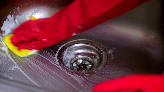 一个女人戴着红手套在厨房里洗金属水槽。视频素材