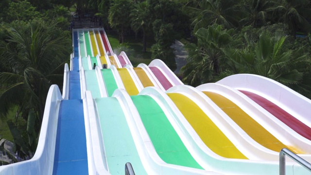 暑假，人们在水上乐园里玩彩色滑水道。人们有乐趣滑梯在室外水上公园在绿色的棕榈树景观视频下载