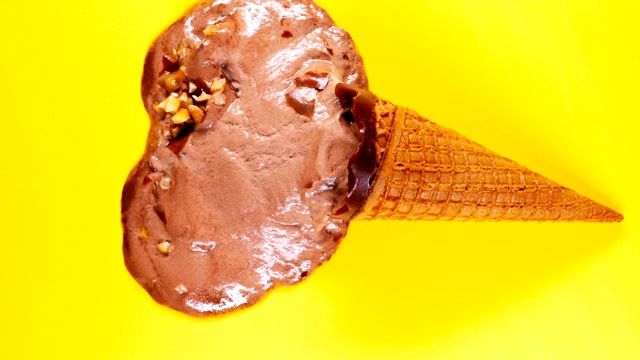 俯视图巧克力口味的冰淇淋甜筒融化在黄色的背景时间流逝视频素材