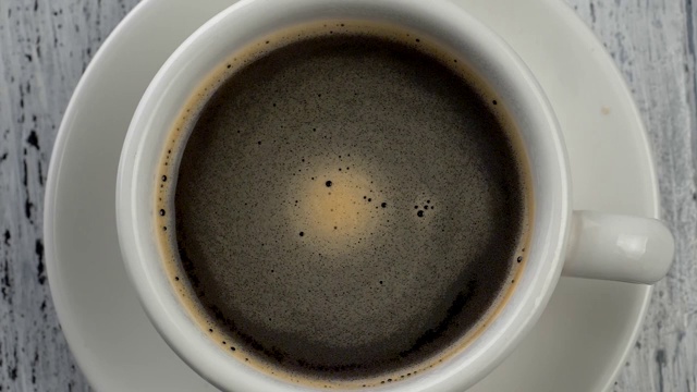 咖啡泡沫在咖啡杯中旋转。破旧的白色木制背景。自顶向下的观点。视频素材