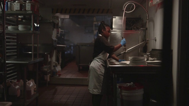一名非洲裔美国妇女在餐馆厨房边洗盘子边唱歌跳舞。视频下载