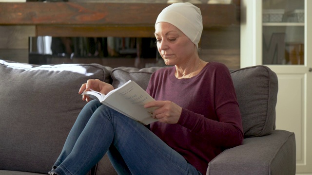 一位身患癌症的老年妇女正坐在沙发上看书。视频素材