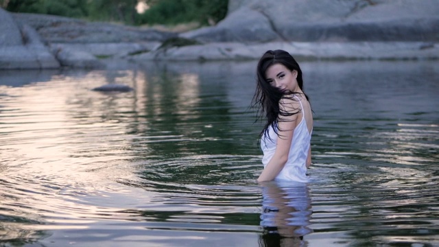美丽的黑发长发女孩站在水里。缓慢的运动。视频下载