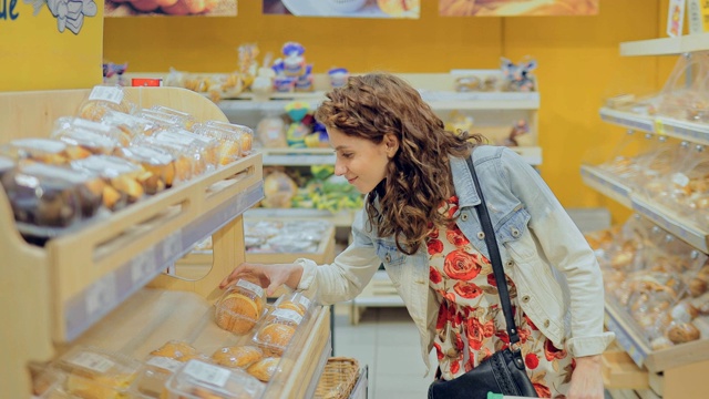 年轻漂亮的女孩在面包店的橱窗里挑选面粉制品。从超市货架上拿甜甜圈的美女。视频素材