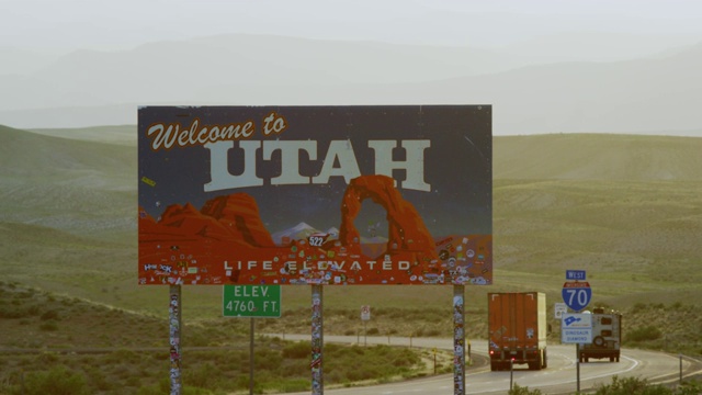 汽车和车辆驶过，从70号州际公路到犹他州/科罗拉多州边界(犹他州东部)上的“欢迎来到犹他州”标志，背景是山脉视频下载