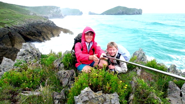 妈妈和儿子穿着雨衣和背包在海岸边以大海为背景自拍视频素材