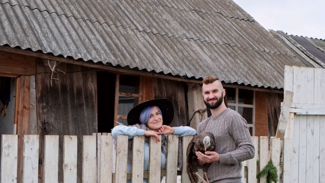 年轻漂亮的男人和女人，已婚夫妇，在一个村庄的农场里，手里拿着一只火鸡。家庭农业。视频下载