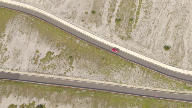 航拍:红色跑车在美丽的意大利阿尔卑斯山上探索弯曲的道路。视频下载