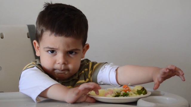 脾气暴躁的两岁小男孩玩食物，拒绝吃东西。视频素材