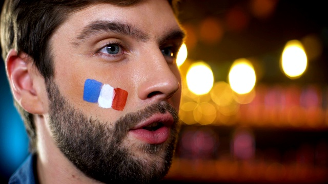 快乐英俊的留胡子的法国球迷与彩旗在脸颊庆祝进球视频素材