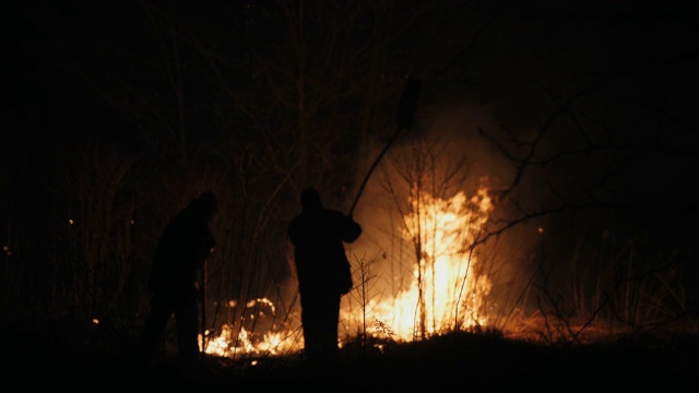 两名消防员在晚上用扑火板扑灭一场火灾视频素材