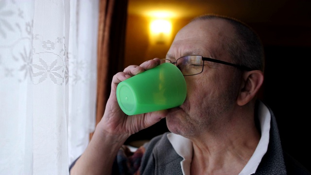 窗边的一位老人吃了一粒药丸，然后用水喝了下去。视频素材