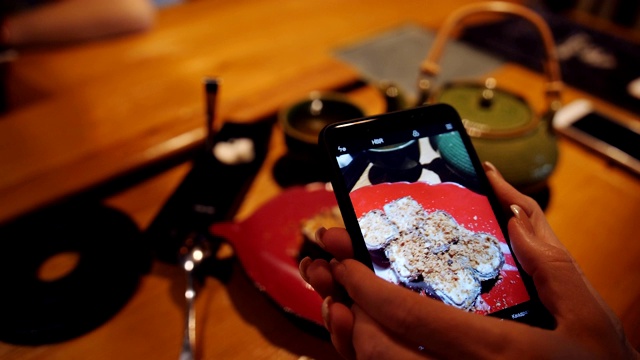 在社交网络上，女孩被智能手机拍到盘子里的甜点和一壶绿茶。视频下载