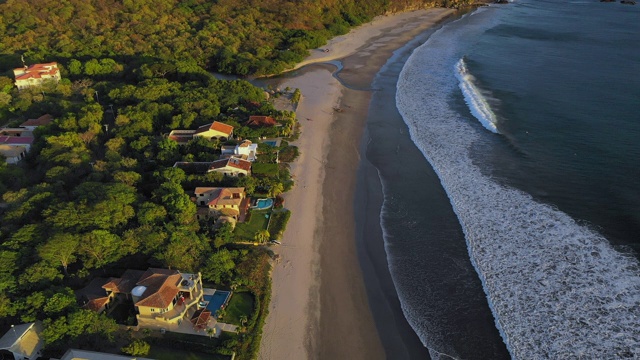 空中向前/右:傍晚阳光下，海滩上房屋和森林的海浪-尼加拉瓜埃尔吉甘特视频素材