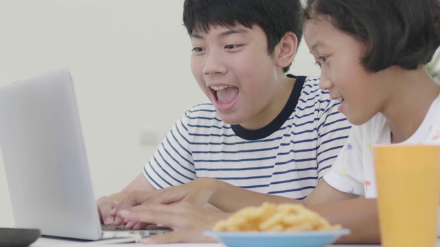 年轻的亚洲男孩和女孩玩笔记本电脑在家里。孩子们一起在笔记本电脑上玩网络游戏。多莉60 fps射击。视频素材