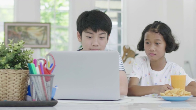 年轻的亚洲男孩和女孩玩笔记本电脑在家里。孩子们一起在笔记本电脑上玩网络游戏。多莉60 fps射击。视频素材