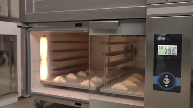 新月形面包卷。工人正在把一个盛有牛角面包的托盘放进烤箱。羊角面包打样。糕点用品、面包店、糕点店。视频素材