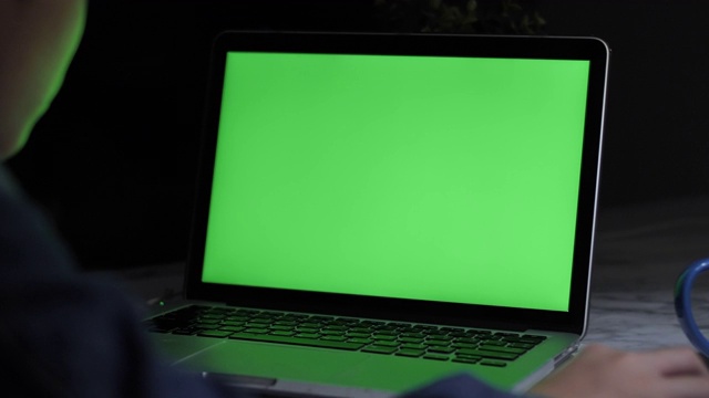 肩上的照片是一个小男孩在桌上使用笔记本电脑，看着绿色的屏幕。多莉60 fps射击。视频素材