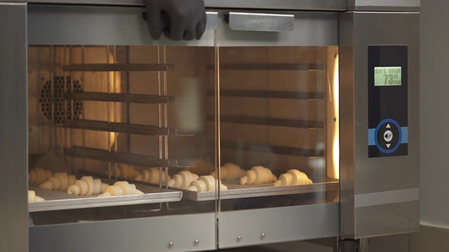 新月形面包卷。厨师将装有牛角面包的托盘放入烤箱进行面团发酵。糕点用品、面包店、糕点店。视频下载