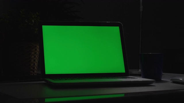 绿屏笔记本电脑。黑暗的办公室。多莉开枪。完美地放上你自己的图像或视频。正在使用的绿屏技术。色度键的笔记本电脑视频素材