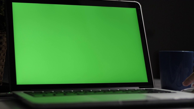 绿屏笔记本电脑。黑暗的办公室。多莉开枪。完美地放上你自己的图像或视频。正在使用的绿屏技术。色度键的笔记本电脑视频素材