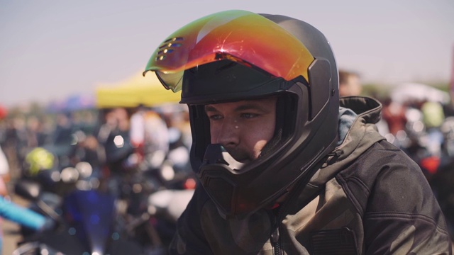 一个骑摩托车的男人在日落时戴着黑色的头盔，在街道上，彩色遮阳板视频下载