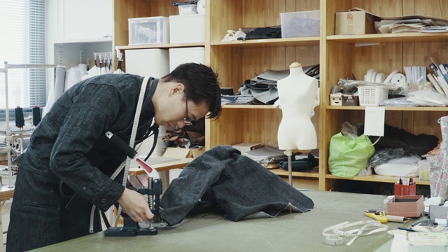 中等拍摄的一个中等成人裁缝工作在他的设计工作室创造牛仔产品视频素材