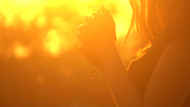 年轻女子在美丽的日落上祈祷十字架视频素材