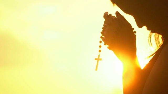 年轻女子在美丽的日落上祈祷十字架视频下载