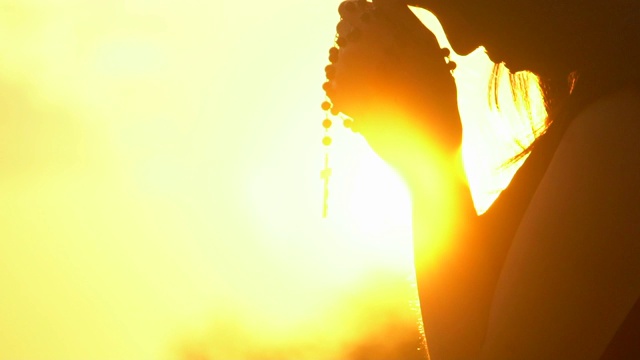 年轻女子在美丽的日落上祈祷十字架视频素材