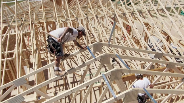 无人机拍摄的白种男性建筑工人在一个阳光明媚的日子里搭建房屋视频素材