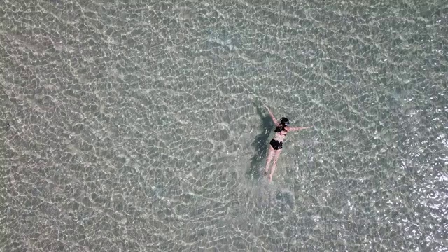 鸟瞰图亚洲妇女游泳和漂浮在水晶清澈的水海上视频下载