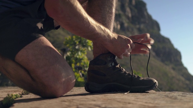 在悬崖上系鞋带的男性徒步者的低部分视频素材