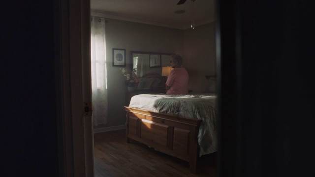 老女人独自坐在床上，凝视着空荡荡的房子里的空间。视频下载