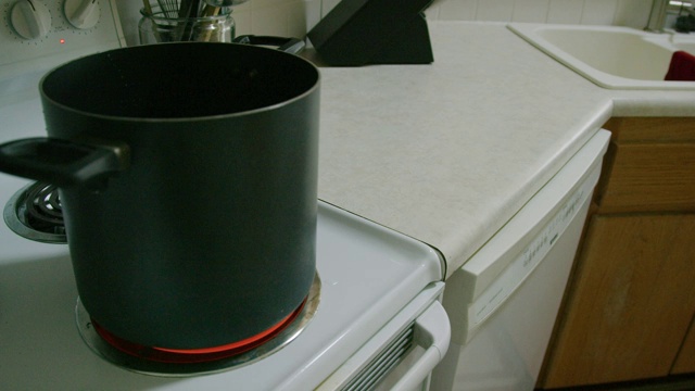 一名白人男子将一个大锅放在厨房里的一个设置为高温的Stop Top Range上视频素材