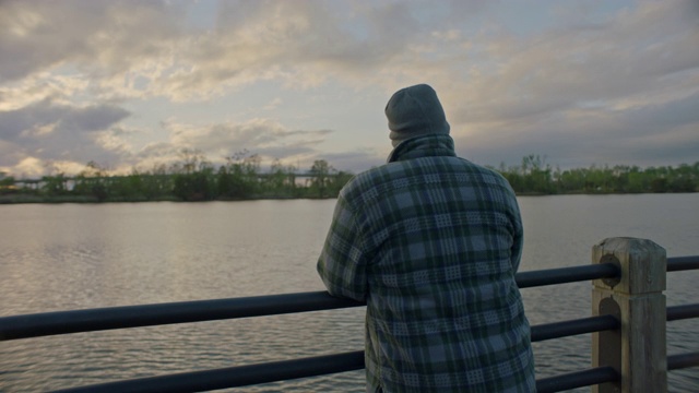 夕阳西下时，一个人站在河边沉思地望着外面。视频素材
