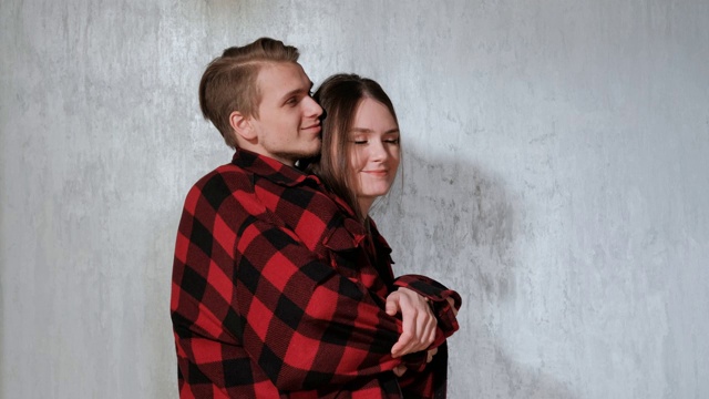 一对年轻美丽的夫妇，男人和女人，在房子灰色的墙上温柔地拥抱着。视频下载